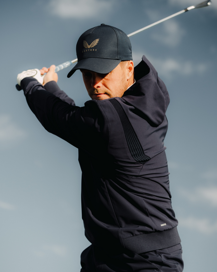 Male golfer wearing Midnight Navy Pinnacle Performance Hoodie mid swing with a cap