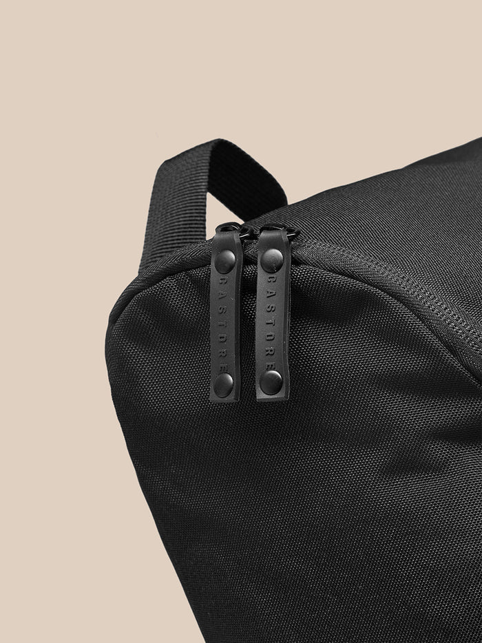 Close-up of black boot bag showing dual zipper pulls on the top corner