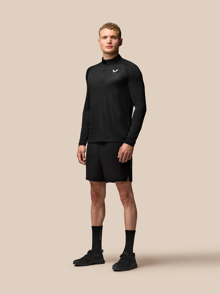 Male model in black Adapt Training 6 inch shorts with matching athletic top against a beige background.
