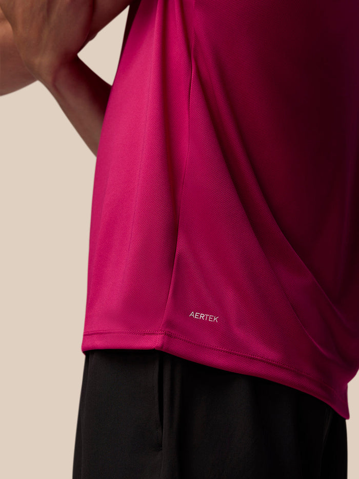 Close-up of pink Adapt Training T Shirt fabric showing AerTek branding at the lower left back hem.