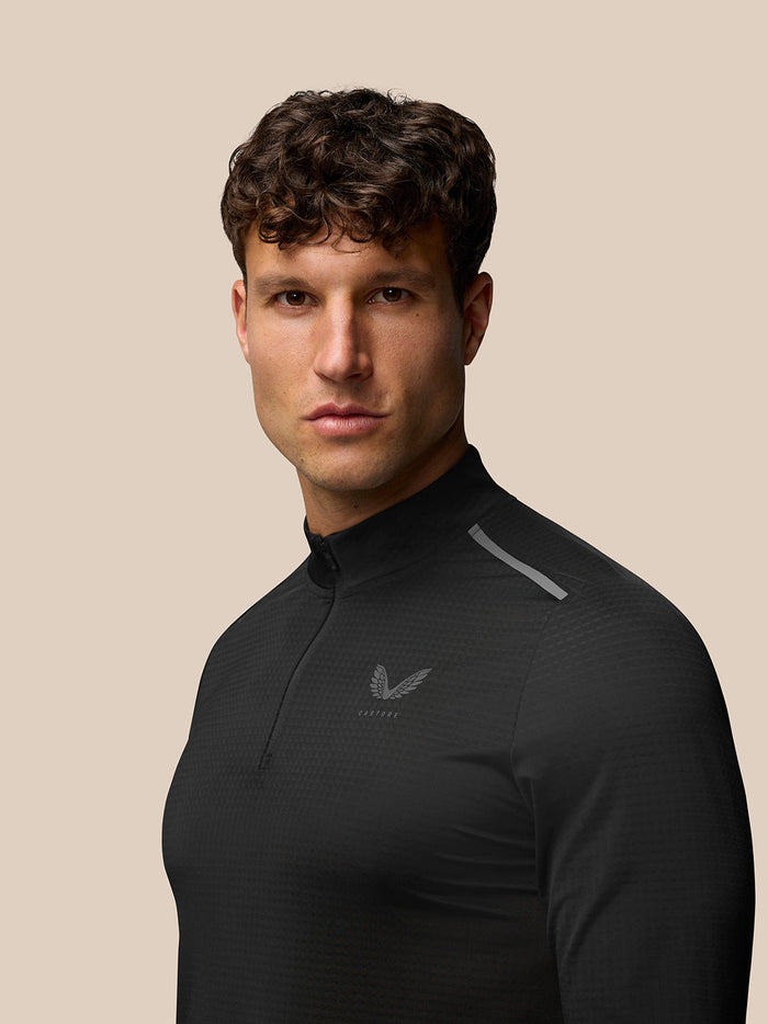 Front view of a man in the black Apex Training Quarter Zip Top with stand collar and reflective branding on the chest.