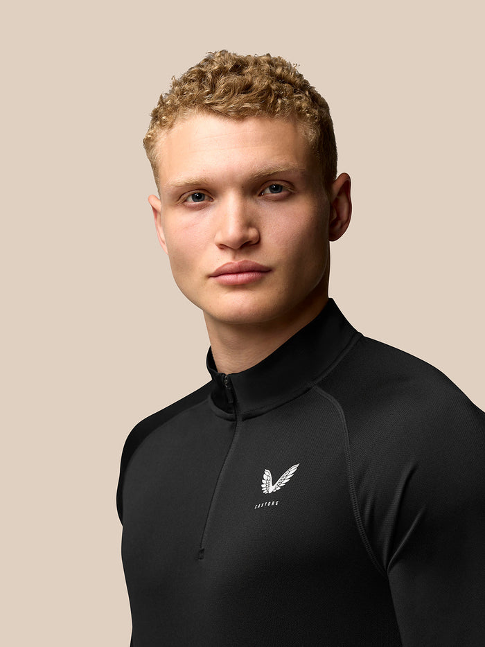 Male model wearing black Adapt Training Quarter Zip Top with stand collar and chest logo