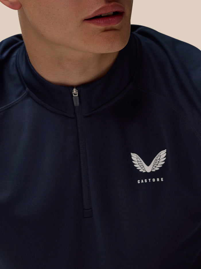 Close up of navy quarter zip top with stand collar and white Castore logo on left chest