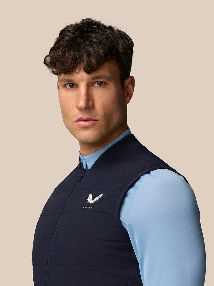 Three quarter view of a man wearing navy Apex Training Gilet showing Castore logo on the left chest.