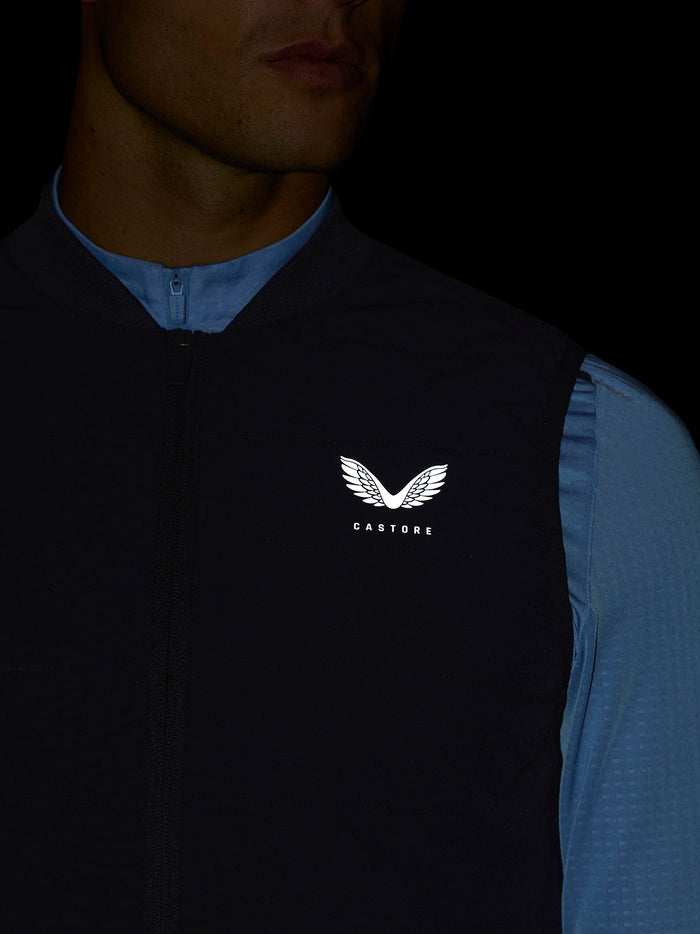 Full-body shot of a man wearing navy Apex Training Gilet over a light blue top, logo on the chest