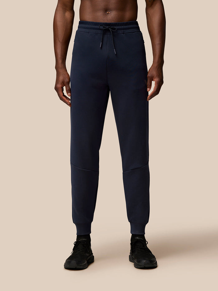 Full length view of a man wearing navy Flex Lifestyle Joggers with a drawstring waist and cuffed ankles, Castore branding on the left thigh