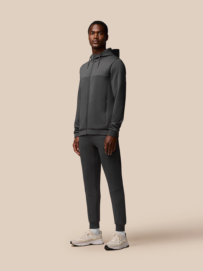 Man wearing charcoal Flex Joggers with matching zip hoodie against a beige backdrop.