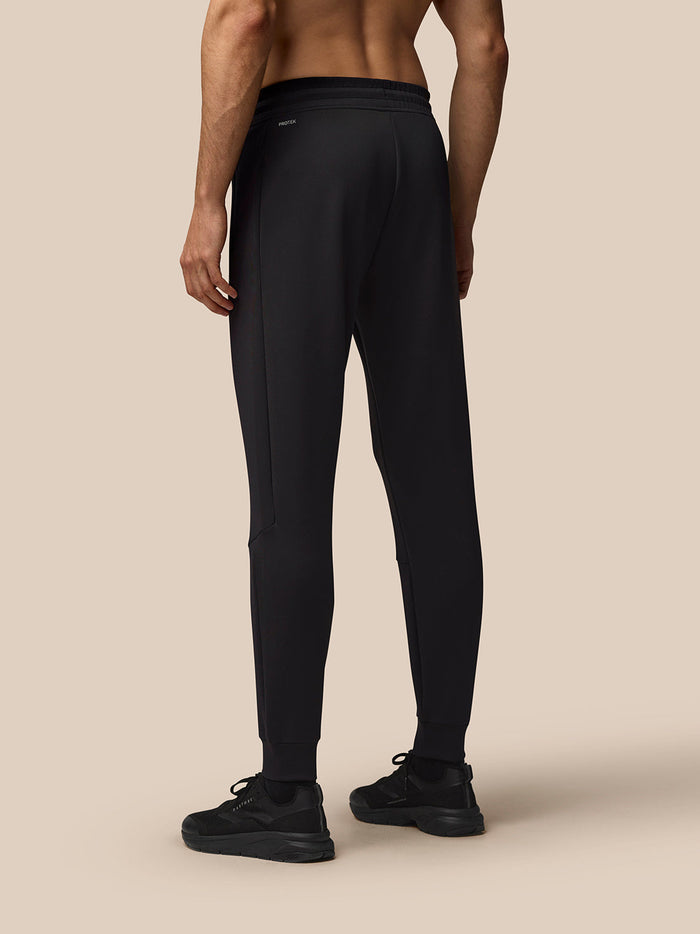 Back view of a man wearing black Flex Lifestyle Joggers with an elastic waistband and cuffed ankles, Protek branding at the left rear.