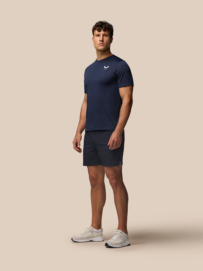 Male model in navy Apex Training T Shirt with shorts and white sneakers photographed in profile