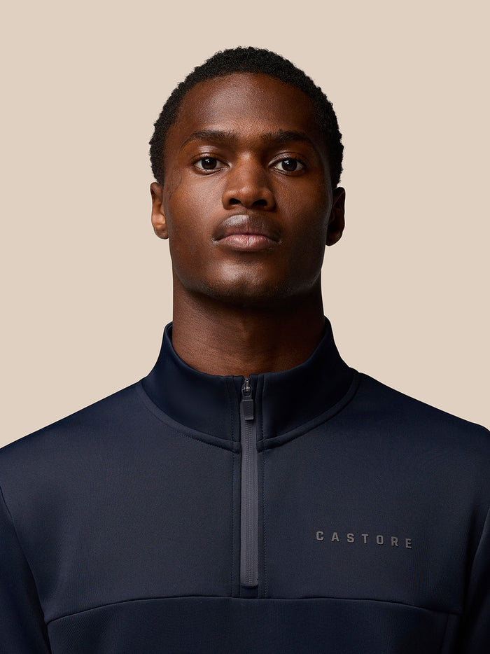 Close-up of navy Flex Lifestyle Quarter Zip top on a model with neck zipper and Castore branding on left chest sleeve and hem