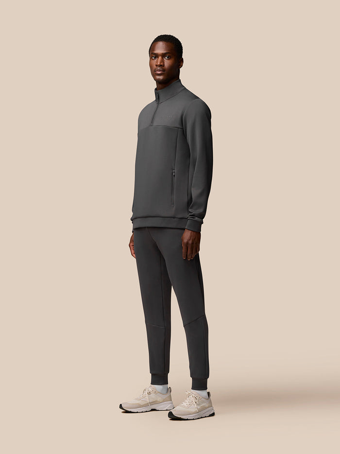 Male model wearing charcoal Flex Lifestyle 1/4 Zip top with zip pockets and Castore branding on chest and sleeve.