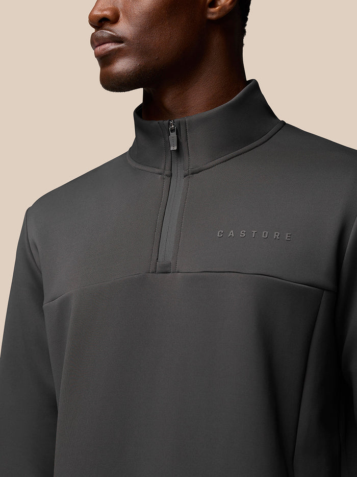 Close up of a man wearing a charcoal Flex Lifestyle 1/4 Zip top focusing on the zip collar and Castore logo on the chest.