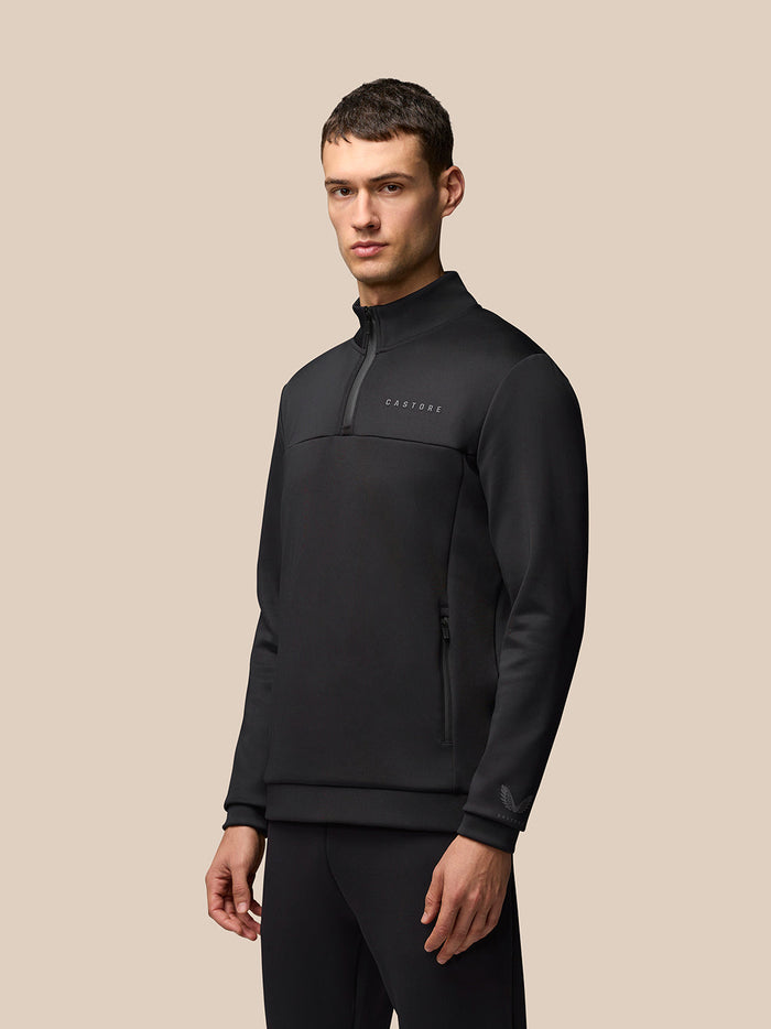 Three-quarter front view of a man in a black Castore Flex Lifestyle 1/4 Zip top with a high collar and left chest logo.