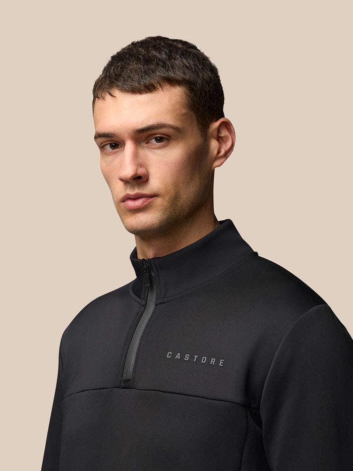 Front left three-quarter view of a man in the black Castore Flex Lifestyle 1/4 Zip top with left chest logo.