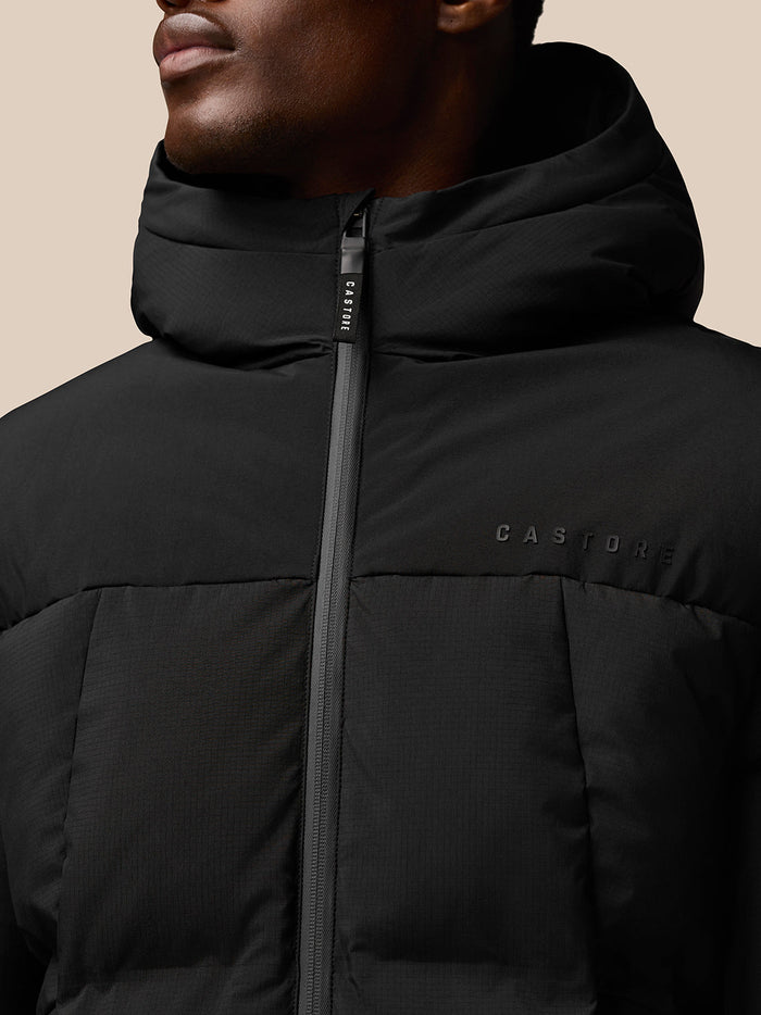 Close up of a black puffer jacket front with a full zip and Castore branding on chest and hood
