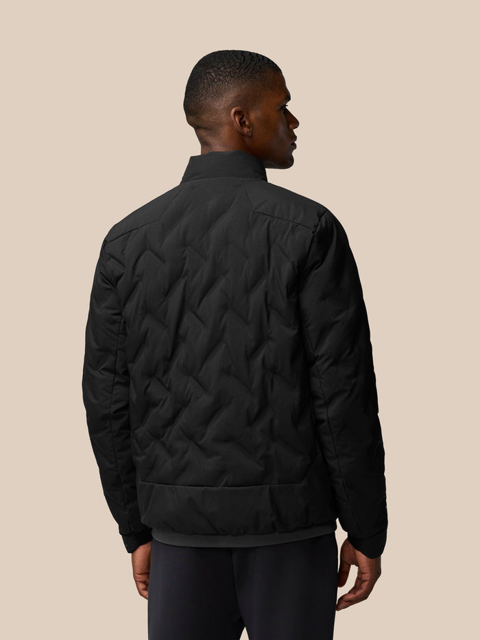 Back view of a man wearing a black padded jacket with chevron quilting and a stand collar.