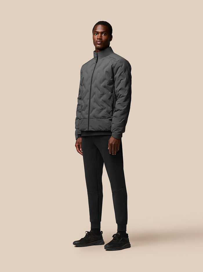 Model wearing charcoal Quilts Lifestyle Jacket with stand collar and front zip, beige backdrop