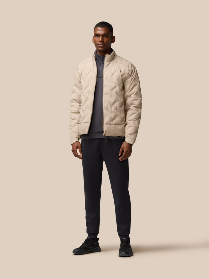 Full-body shot of man wearing Mushroom padded jacket over a grey top, standing against beige backdrop