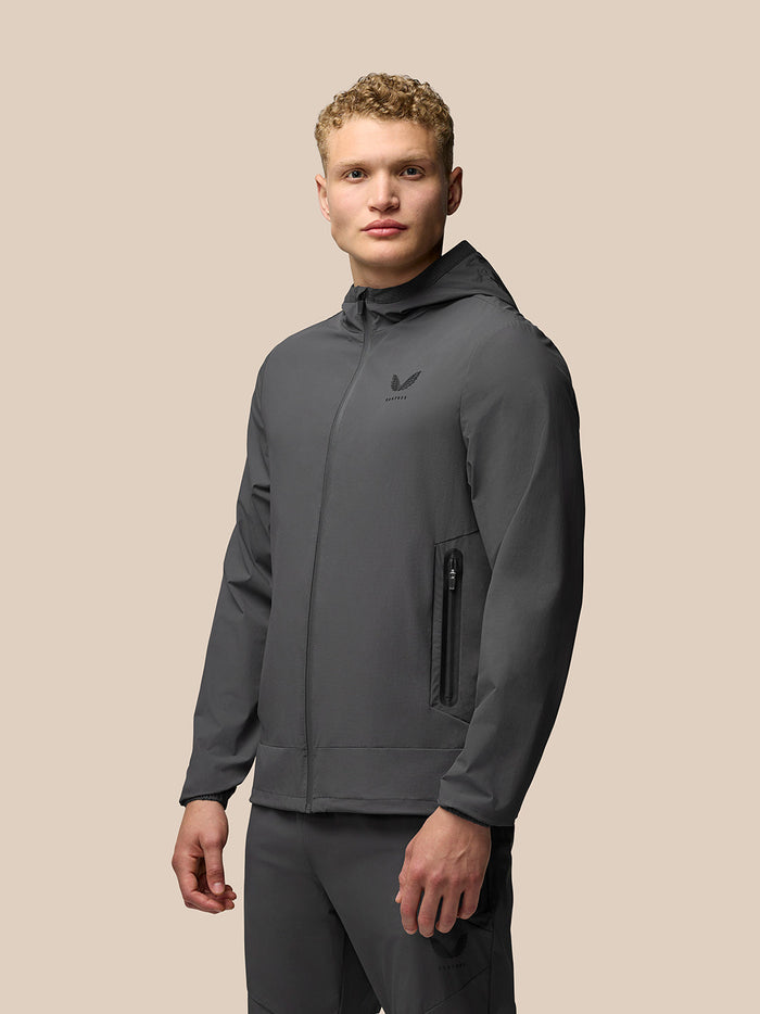 Model wearing charcoal Lightweight Flex Jacket with hood, full front zipper and left chest branding.