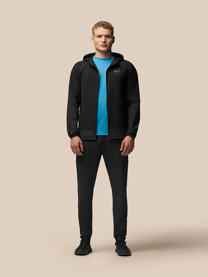 Full-body shot of a male model in the black Flex Winterised Jacket with hood over a blue top