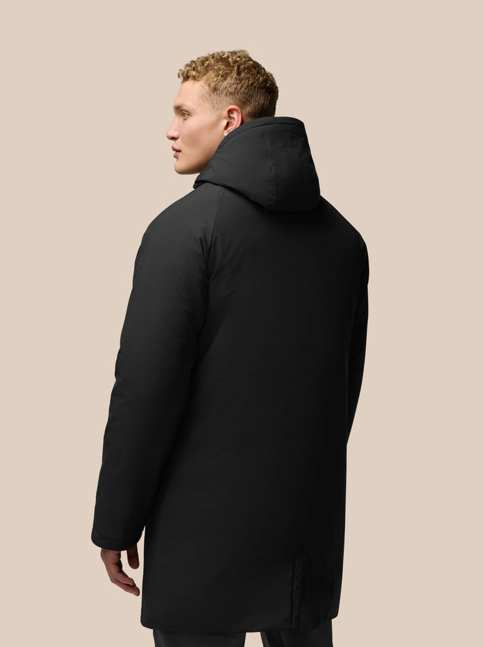 Back and side view of model in black longline wadded jacket with hood, showcasing hood fit and silhouette.