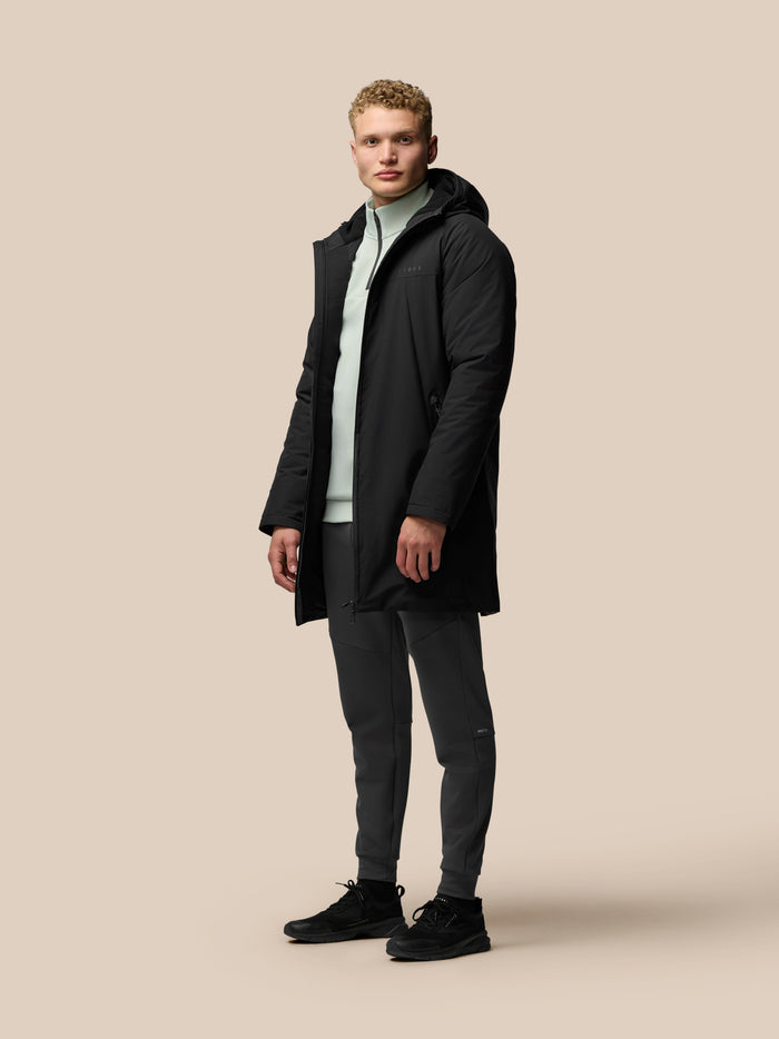 Three-quarter view of model in black longline wadded jacket unzipped to reveal mint lining and chest logo.