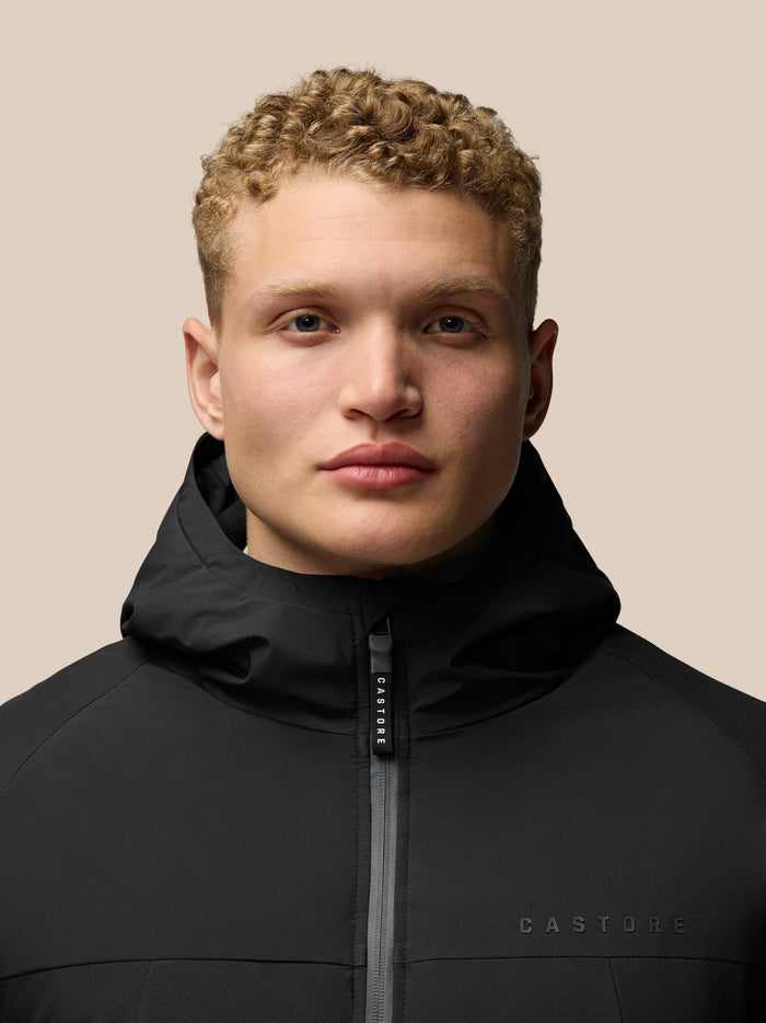 Close-up of a model wearing the black Longline Wadded Jacket with hood and front zipper.