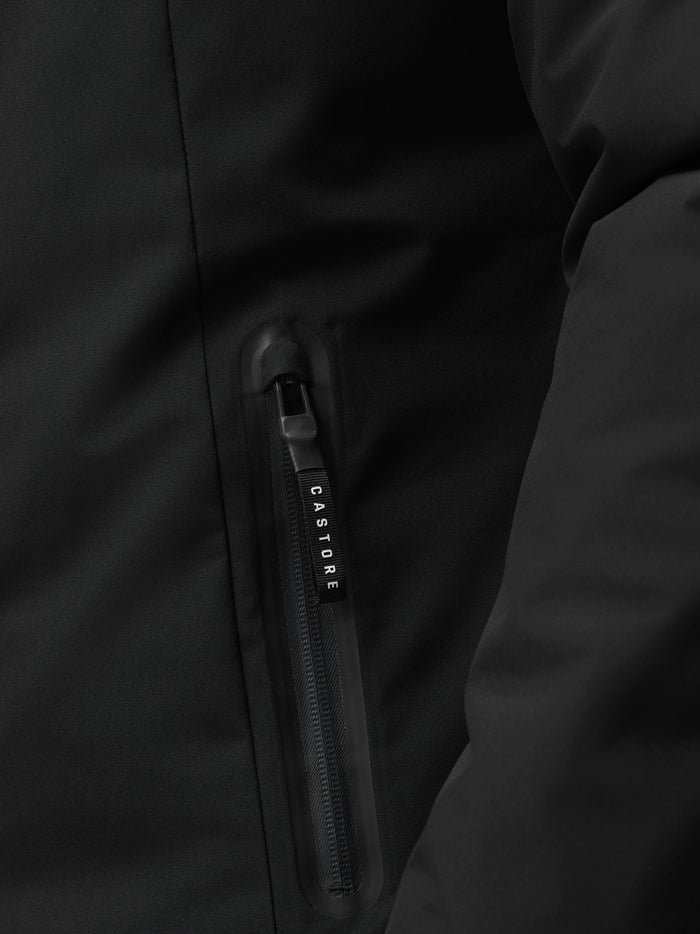 Close-up of black longline jacket showing waterproof zipper pull with Castore branding.
