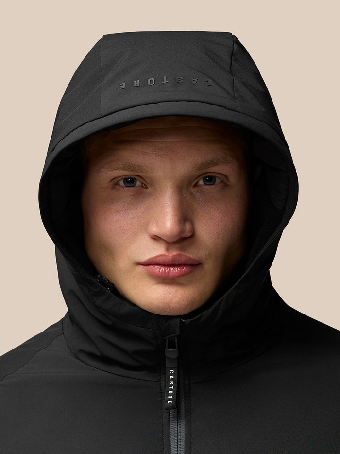 Portrait of a model wearing a black hooded jacket with Castore branding on the hood and zip