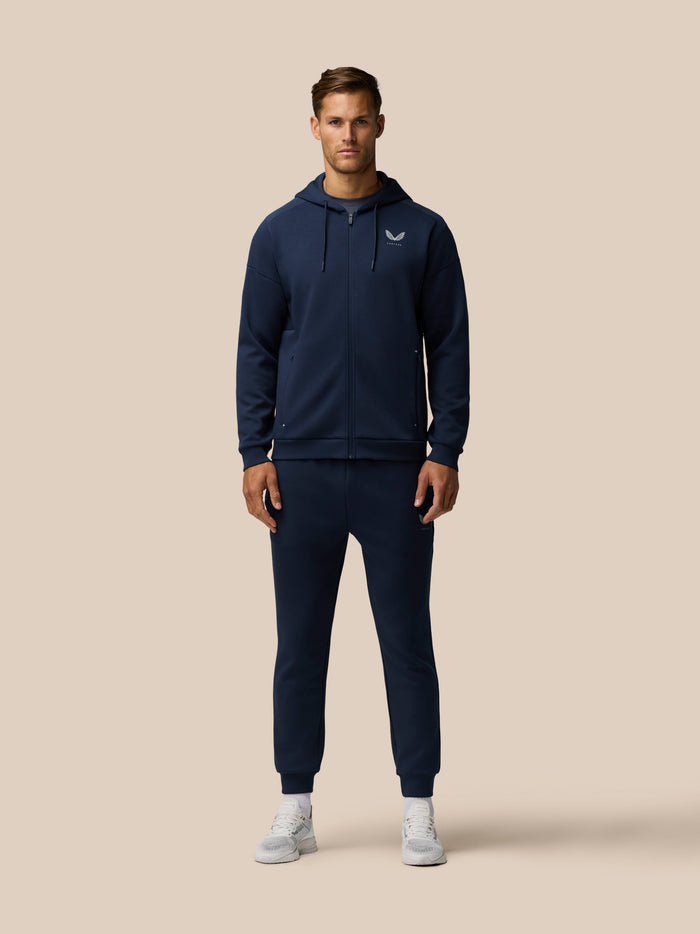 Male model wearing navy Travel Lifestyle Joggers with matching zip hoodie and Castore logo on the chest