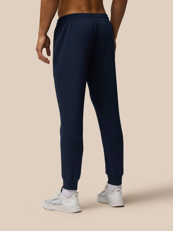 Rear view of a model wearing navy Travel Lifestyle Joggers with elastic waistband and cuffed hems, white sneakers.