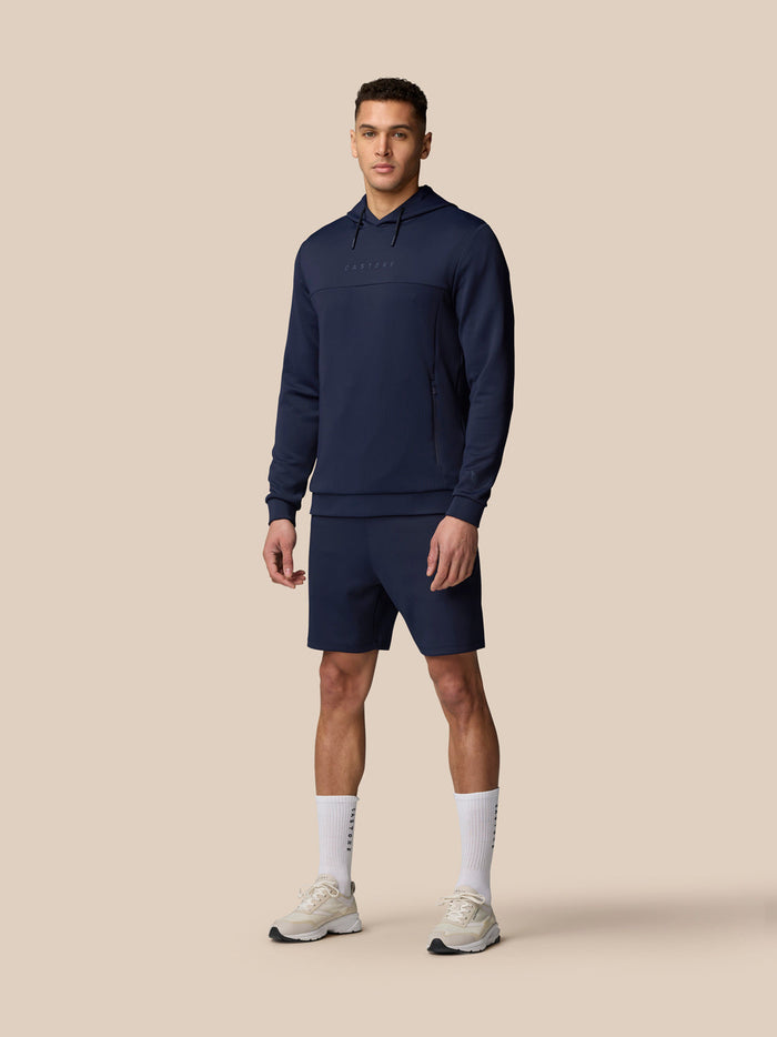 Male model in midnight navy Flex Lifestyle shorts with a matching navy hoodie against a beige backdrop