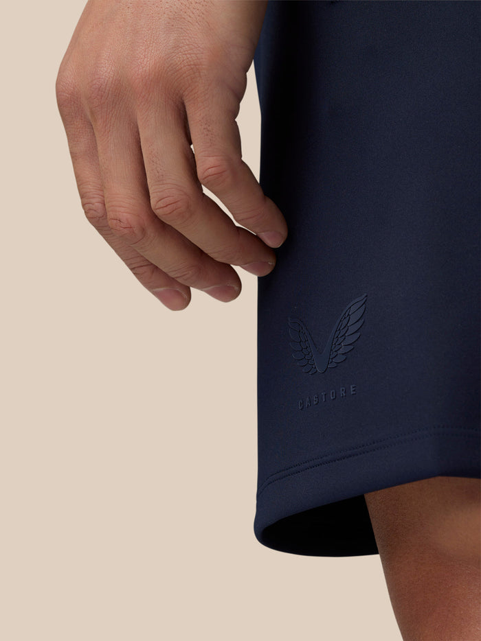 Close-up of navy shorts hem with embossed Castore logo and a resting hand
