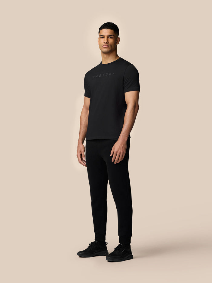 Full-body shot of male model in black graphic T-shirt with Castore logo paired with black joggers and sneakers