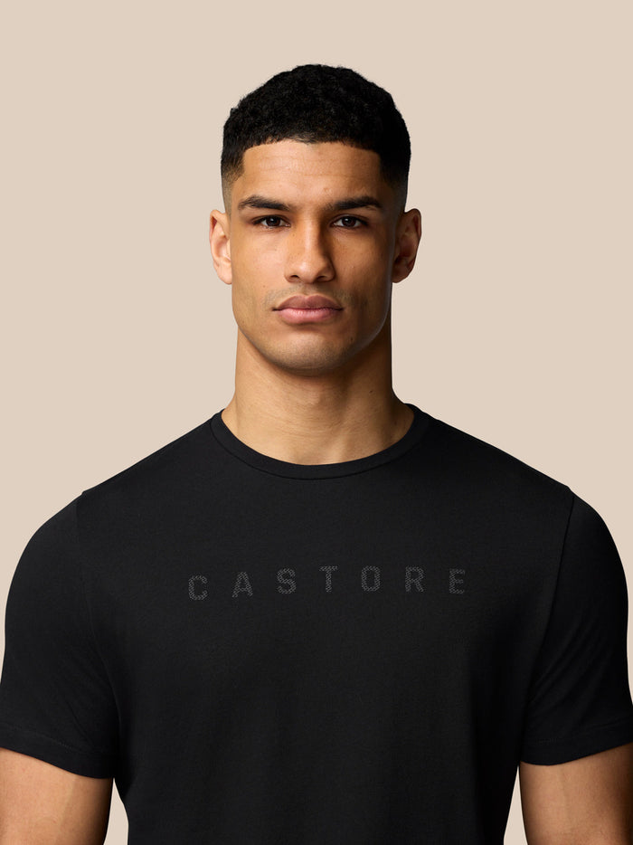 Close up of a model wearing a black Castore graphic T shirt with a subtle logo across the chest.