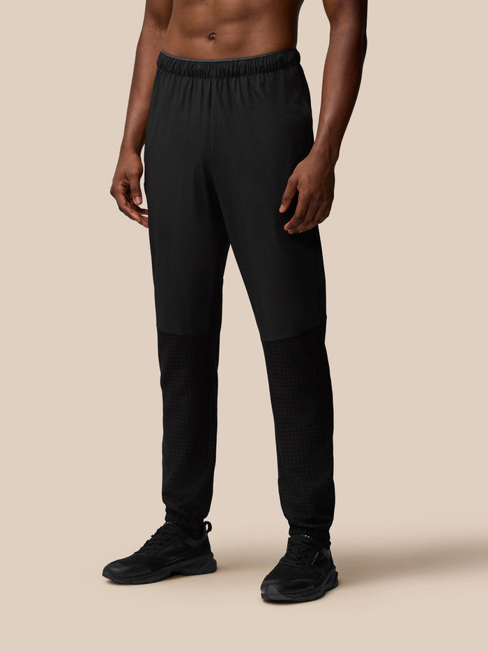 Front view of a man wearing black Flex Winterised Woven Joggers with elastic waist and textured lower panels.