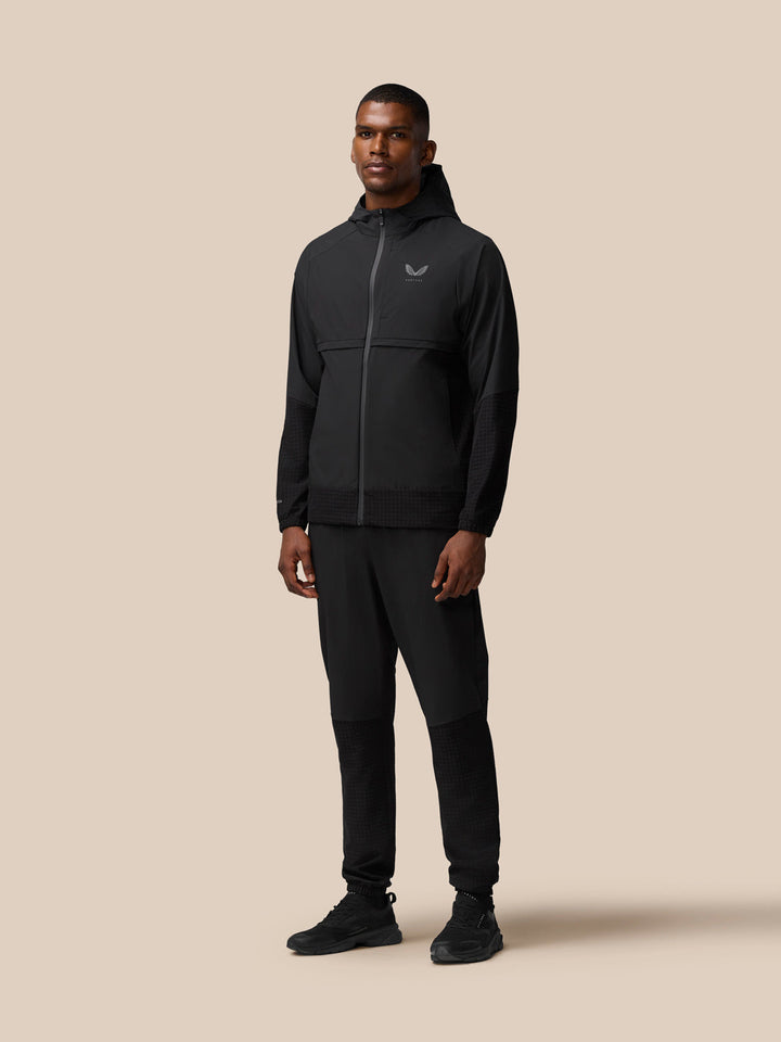 Full body view of a man wearing black Flex Winterised Woven Joggers with a black jacket.