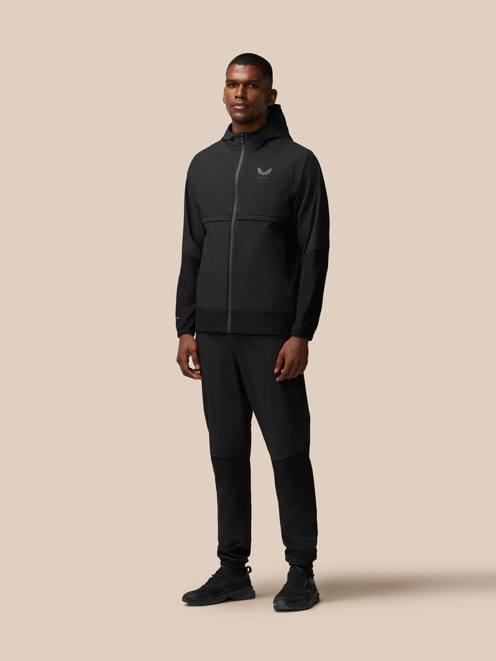 Full body view of a man wearing black Flex Winterised Woven Joggers with a black jacket.