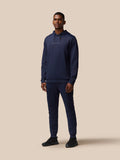Male model wearing navy Castore Flex Lifestyle Thermo Pant tracksuit with hoodie, full-body view.