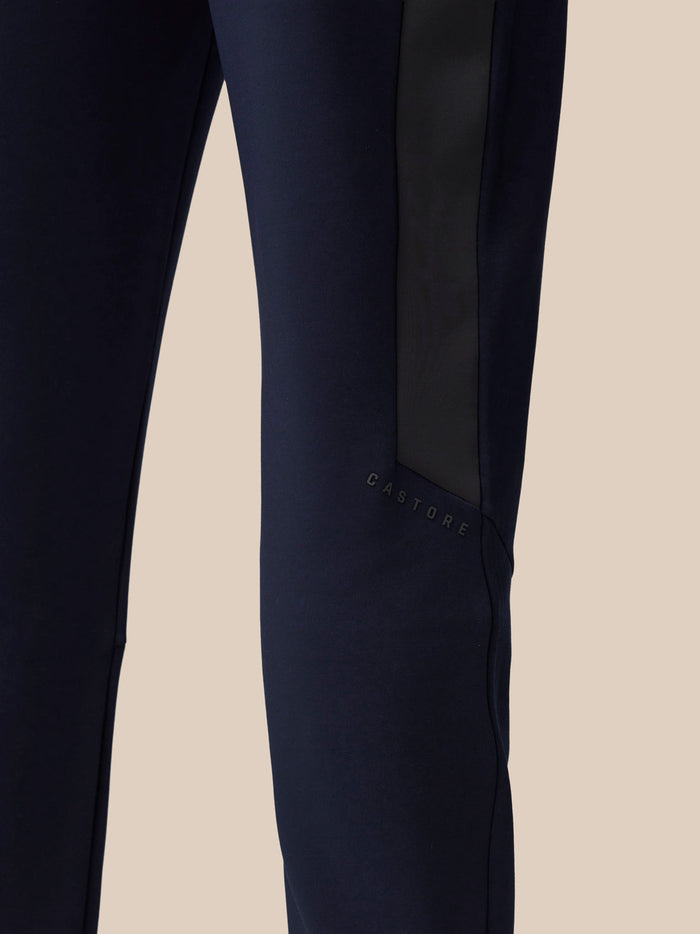 Full-body view of man in navy Flex Thermo Pant tracksuit with side stripe and Castore logo on the leg.