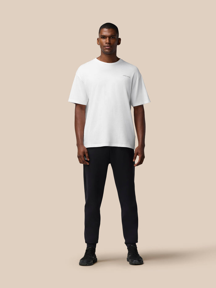 Back view of a male model in a white T shirt with black joggers on a beige backdrop