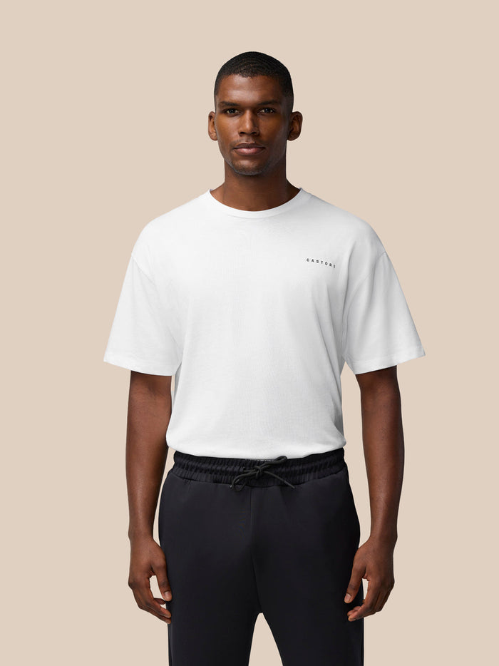 Front view of a male model in a white Flex Cotton T-shirt with small chest logo and black joggers on a beige backdrop