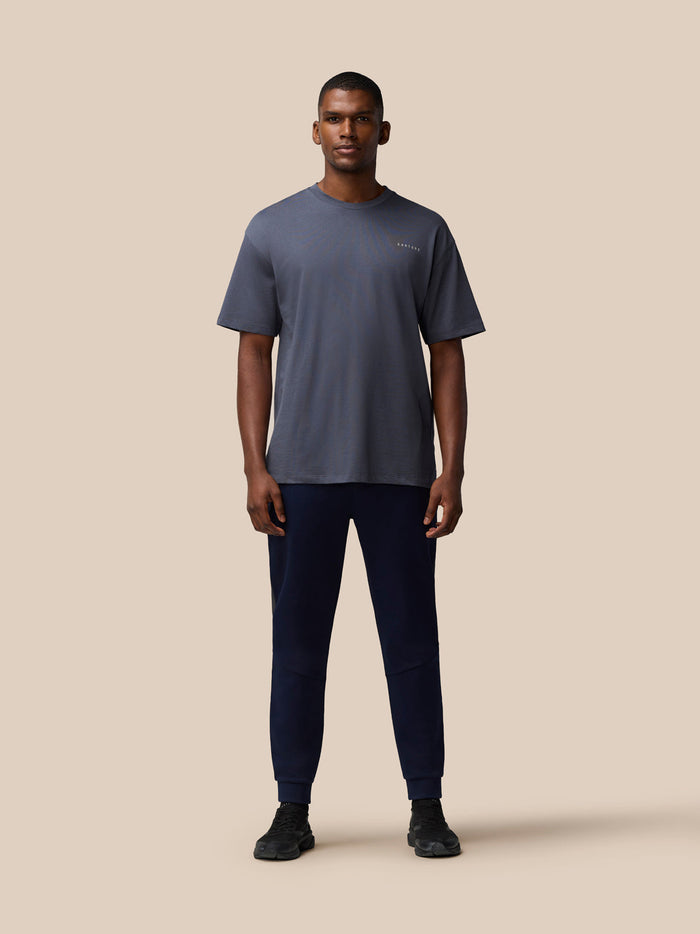 Full-body front view of a man wearing a pewter gray Flex Cotton T Shirt with a round neckline and navy joggers