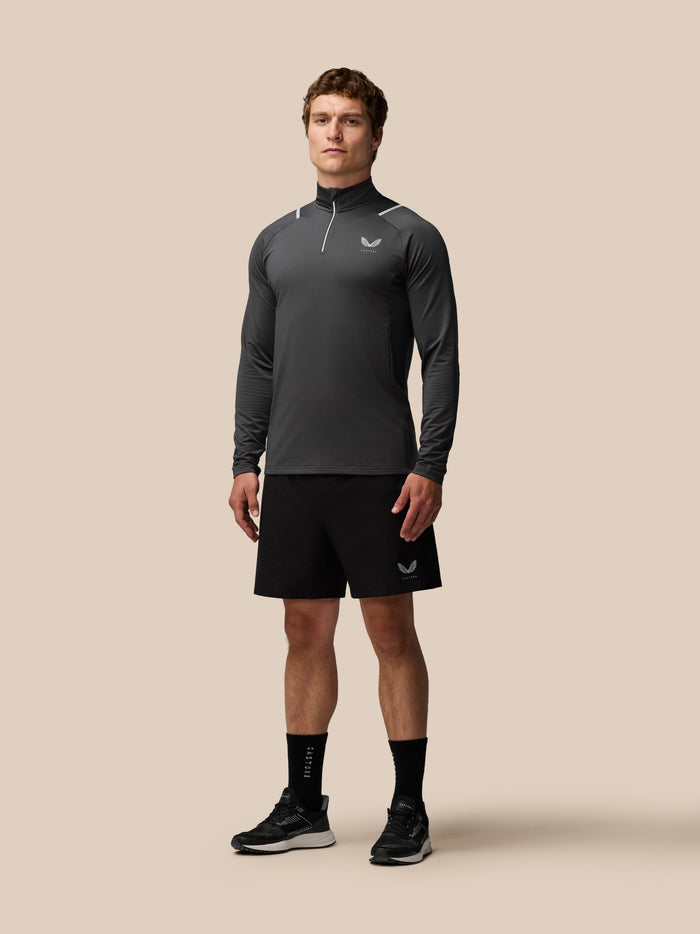 Model in charcoal Apex Training Winterised quarter zip top shown from side with high collar and reflective piping.