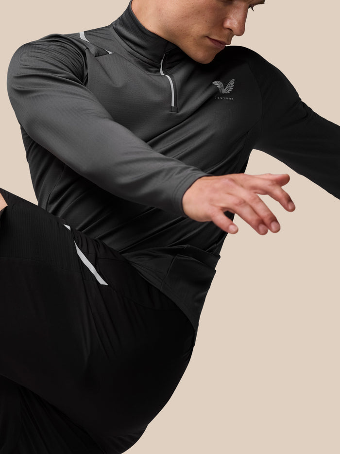 Close-up of a man wearing charcoal Apex Training Winterised 1/4 Zip Top with reflective zipper trim and Castore wing logo.