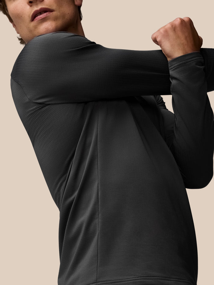 Close-up of a model wearing a charcoal Apex Training top, highlighting the textured sleeve and shoulder seam against a beige background.