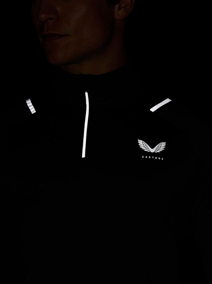 Close-up of a person wearing charcoal Apex Training Winterised 1/4 Zip Top with reflective piping and a winged Castore logo on the chest