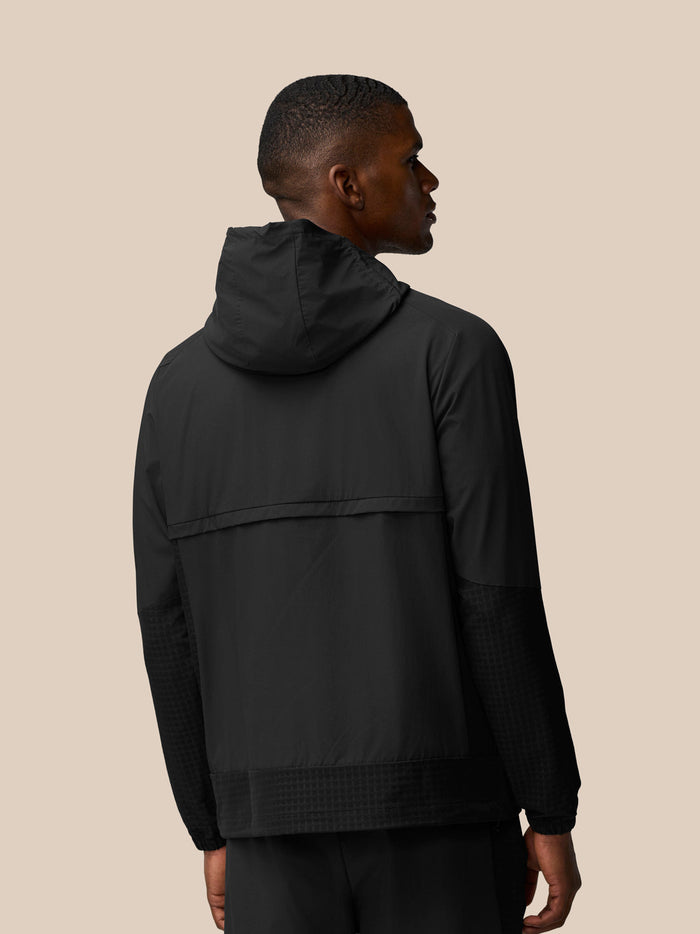 Back view of black Flex Winterised Woven Jacket on model, hood up, showing shoulder seams and textured sleeve panels.