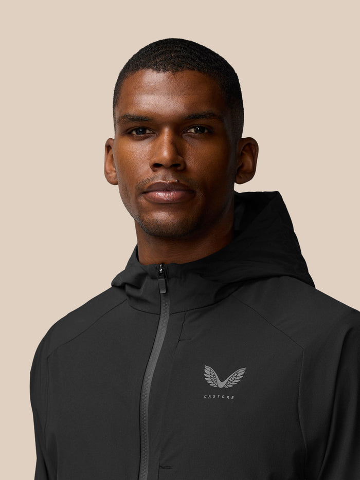 Close up of a man wearing a black Flex Winterised Woven Jacket with the Castore logo on the left chest.