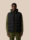 Male model wearing black heavyweight padded gilet over olive green hoodie against a beige backdrop